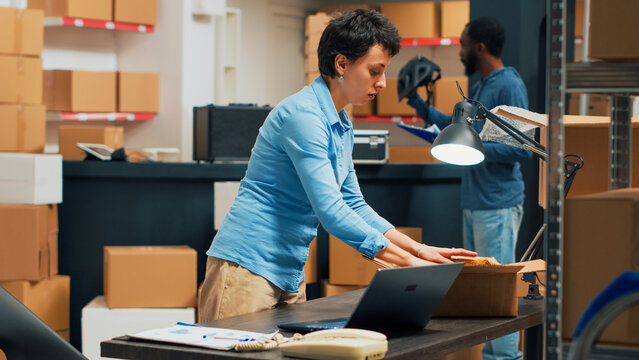 Small business owner putting supplies in cardboard boxes, shipping merchandise to customers. Young woman preparing shipment with warehouse goods, retail and logistics. Tripod shot.