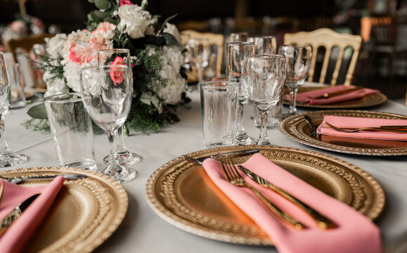 Elegante mesa de evento decorada con vajilla dorada, copas y flores en tonos rosados