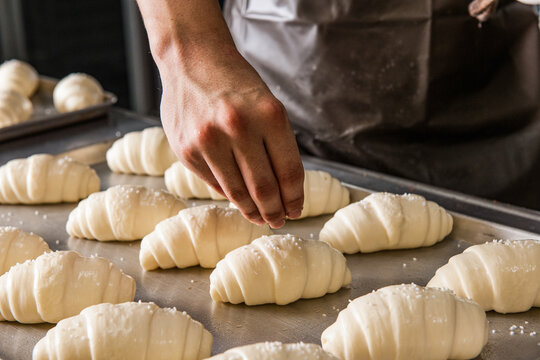 Bread Making Process: Baker Sprinkling Sea Salt over Raw Salt Bread Dough on a Baking Sheet