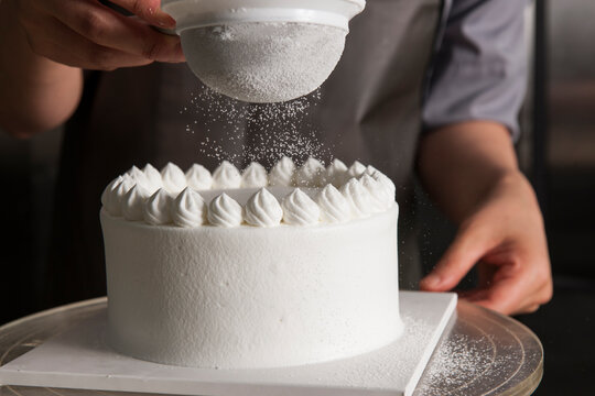 Cake Making Process: Pastry Chef Sifting Powdered Sugar over a Fresh White Cream Cake