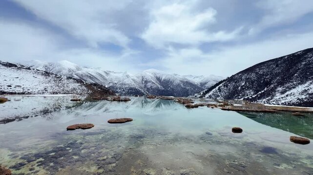 Stunning 4K time-lapse of moving clouds over snow-capped peaks reflected in the crystal-clear water of a high-altitude Tibetan lake at dawn.