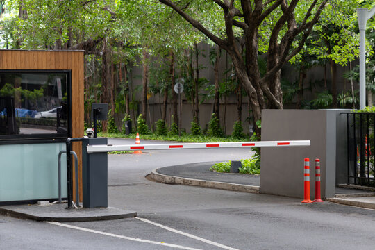 Driveway security gate with automated barrier arm, guard booth, and greenery