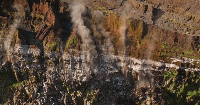 Aerial view highlighting the rugged, layered rock formations and volcanic steam rising from the inner wall of a large caldera on Ambrym Island, Vanuatu. Natural background. Drone flight panorama