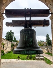 Fototapeta premium Ancient Bronze Bell Hanging in Stone Archway with Garden Background.