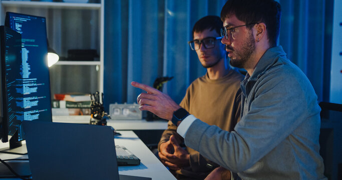 Team adult male engineer collaborate on robotic hand project using AI code solutions machine learning at tech workspace night. Artificial intelligence interface, collaboration prototype development.