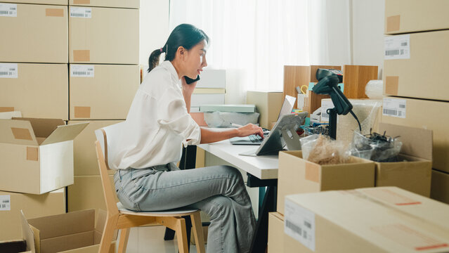 Youth attractive Asia female entrepreneur small business start up call smartphone confirm order with customer confirm check stock inventory product ready for delivery shipment at online retail shop.