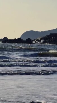 A vertical perspective of the East China Sea coast featuring dark rocky formations and distant mountains at dusk near Putuoshan, Zhejiang.