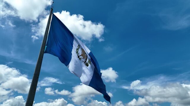 Guatemala flag waving in a blue sky with clouds - orbit with drone