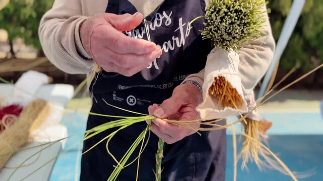 Close up of elderly farmer hands weaving esparto grass braid. Traditional craft, rural lifestyle, handmade work, texture and detail of artisan skill.