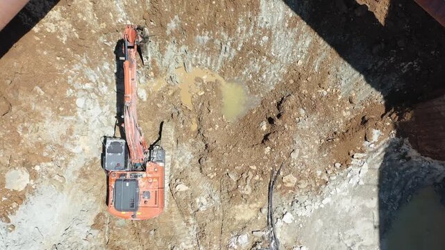 Drone shot of excavator and ground improvement machine working under steel strut pipes in deep foundation excavation. Shoring systems in engineering and heavy industry.