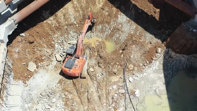 Drone shot of excavator and ground improvement machine working under steel strut pipes in deep foundation excavation. Shoring systems in engineering and heavy industry.