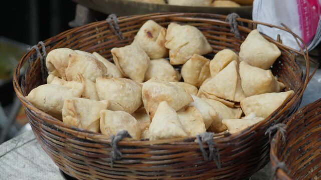 Crispy Samosas with potato filling in woven basket selling at food stall at Kolkata street local shop, popular Indian snack with tea.