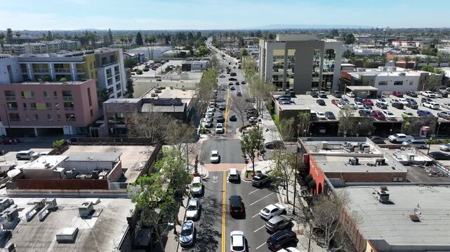 Aerial drone view of Downtown Downey, California, showcasing a mix of stores, restaurants, and bars on a sunny day. The footage highlights busy streets, local businesses