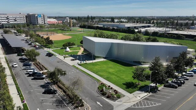 Aerial drone view of the space museum in Downey, California, located within a park alongside a soccer field on a bright, sunny day. The footage captures the unique structure, open green space