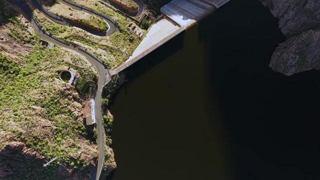 Breathtaking top down aerial shot revealing the Parralillo dam and reservoir next to a curvy mountain road in Gran Canaria, Canary Islands