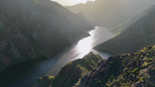 Majestic aerial view of the Parralillo reservoir nestled between mountains in Gran Canaria. The sun reflects off the tranquil water