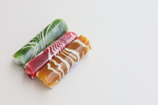 Three pieces of Dodol Garut, traditional Indonesian sweet taffy, with colorful striped patterns in red, green, and brown, isolated on a white background.