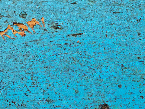 Weathered turquoise painted wood surface with peeling orange paint revealing aged grain texture and scratches under natural light showcasing rustic decay and time-worn character for design or