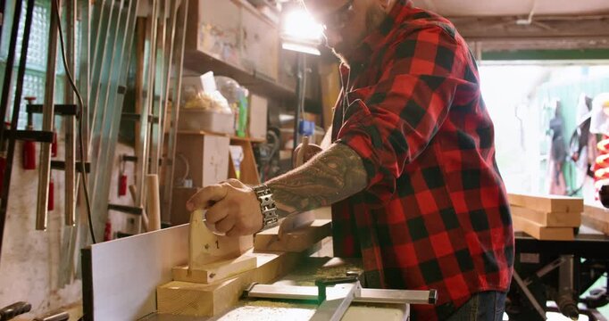 Carpenter occupation. Jointer machine. Handyman in workshop interior processing fresh cut plank on professional electric equipment.
