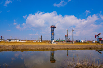 Obraz premium Oil pump in operation with blue sky and white clouds