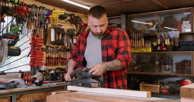 Sanding wood. Carpentry tool. Joiner man smoothing plank surface with professional belt sander equipment in garage workshop interior.