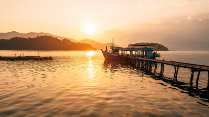 Fototapeta premium Traditional Thai wooden fishing boat moored at a pier during a golden sunset.