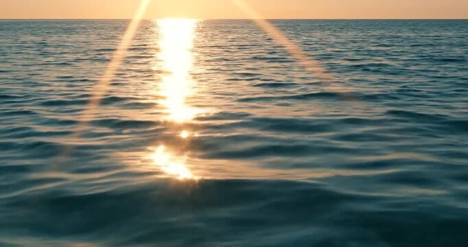 Golden sunset light reflecting on calm blue ocean surface waves at dusk