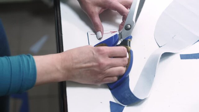 Cutting garment. Tailor process. Professional female hand creating clothes according to paper draft working with scissors on white table