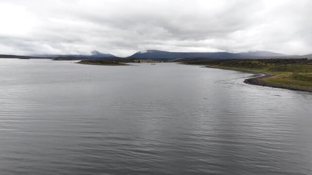 Cinematic flying forward across the grey, moody waters of the Beagle Channel toward the remote bay of Bahia Harberton and the rugged Tierra del Fuego mountains