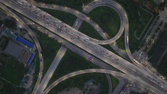 Symmetrical aerial shot of multilayer highway intersection with circular ramps and continuous traffic movement in Hanoi urban environment during twilight hours