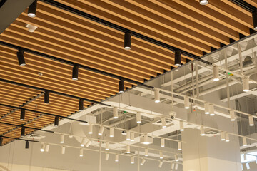 Fototapeta premium Modern ceiling with wooden slats, lighting system and CCTV camera in commercial interior, showing industrial architectural design, captured from low angle