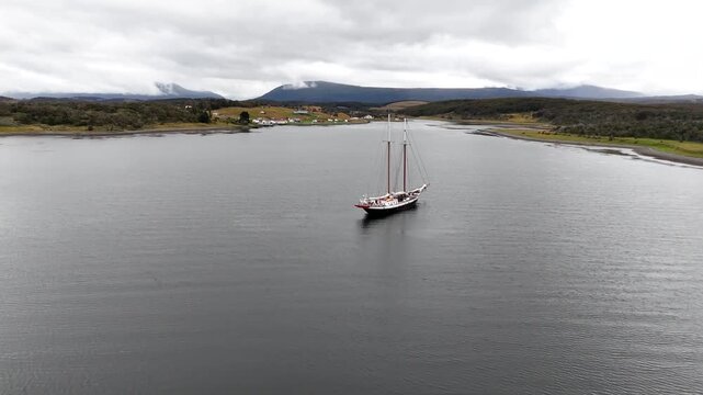 Cinematic fly-past of the two-masted Schooner Amazone anchored in the Beagle Channel, with the historic Estancia Harberton and Tierra del Fuego mountains in the background