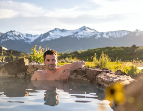 Man relaxing in natural hot springs with stunning mountain backdrop.