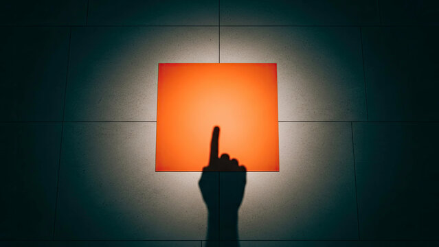 Finger pointing at illuminated orange square, shadow hand concept, dark room.
