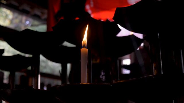 Slow motion close-up of a candle flame burning a glowing light inside a small prayer spiritual shrine at Fushimi Inari Shrine hiking forest trails in Kyoto traditional city Japan history and tourism