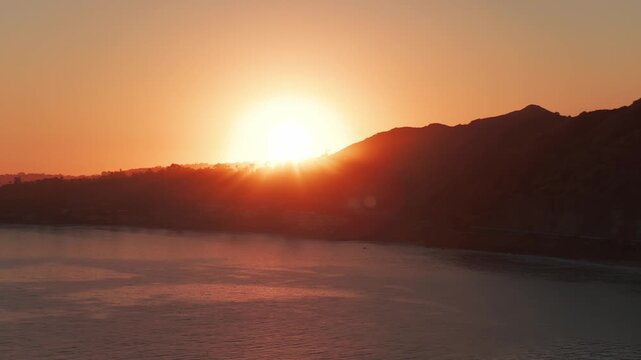 Telephoto dolly aerial shot of the sun setting over Point Dume in Malibu, California. 4K