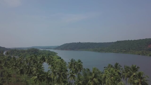 Aerial view of a tranquil tropical waterway meandering past coconut groves and verdant hillsides in coastal Konkan region of Maharashtra, India.