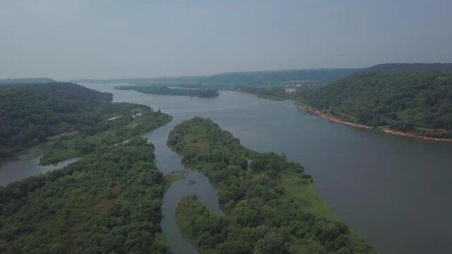 Karli River backwaters wind through lush green forested islands and hills near Devbag in Malvan, Maharashtra, India, with calm water channels and dense tropical vegetation visible under overcast.