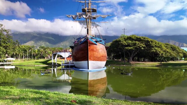 Low angle camera movement over green grass tilting up to show the historic ship inside a sunny public park