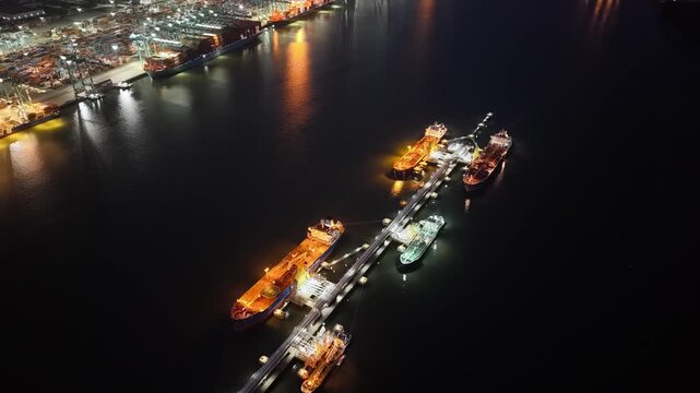 Illuminated aerial night view of crude oil terminal with tankers and dock operations at port.