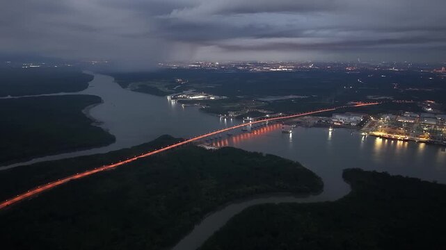 Drone aerial night view of illuminated Pulai Bridge and river landscape under moody storm clouds.