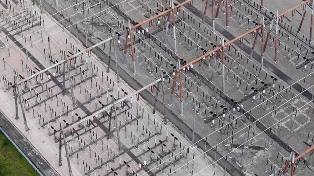 Drone aerial view of high-voltage substation with transmission lines, transformers, and industrial grid infrastructure.
