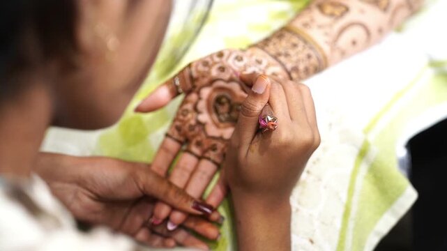A girl drawing mehendi design on the hands of an Indian bride
