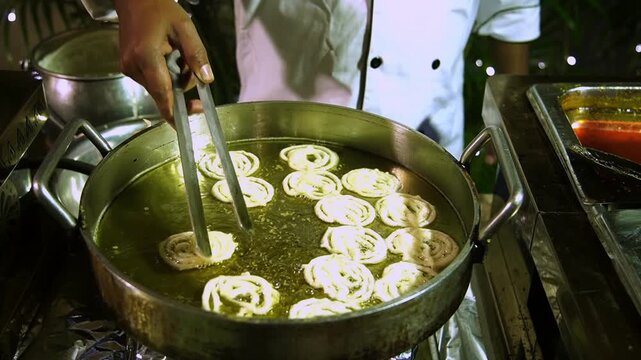 A professional Indian halwai preparing fresh, hot jalebis at a live dessert counter during a grand traditional wedding celebration