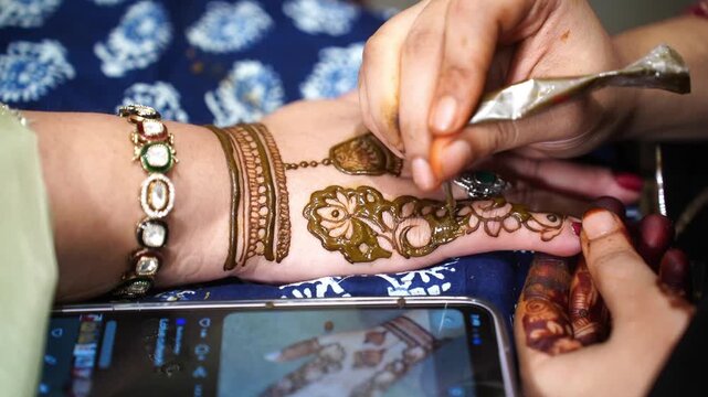 Modern Mehendi application: A young Indian woman following an intricate henna design from a smartphone screen during a festive celebration