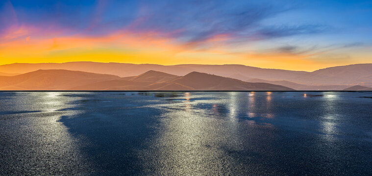 Wet asphalt road reflecting vibrant sunset colors over rolling hills landscape