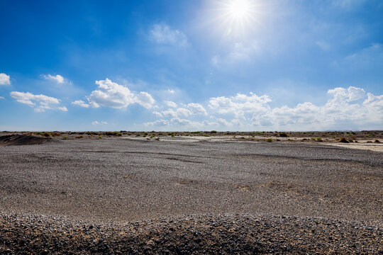Low angle view of sandy ground with a bright sunburst and lens flare in a clear blue sky