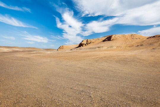 Vast sand dunes in the desert under a bright blue sky with wispy clouds, Xinjiang, China. Scenic arid landscape.