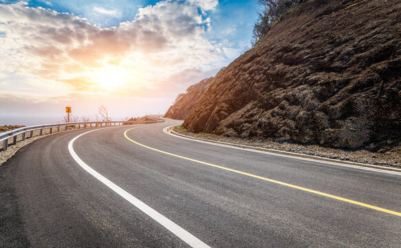 Winding asphalt mountain road with safety guardrail at sunset. Scenic curvy highway during golden hour