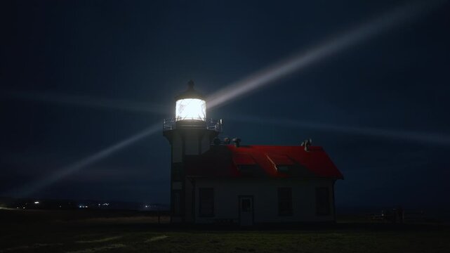 Foggy night lighthouse illuminating Pacific coast landscape near Mendocino, California, USA, with bright beacon casting long light rays across dark sky and ocean